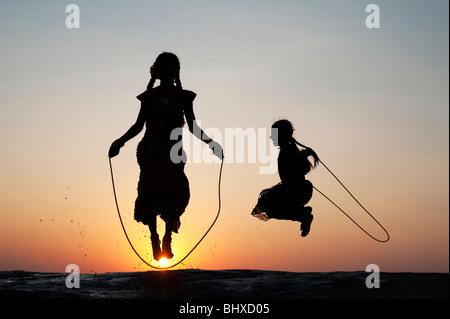 Silhouette di giovani ragazze indiano saltando in acqua al tramonto. India Foto Stock