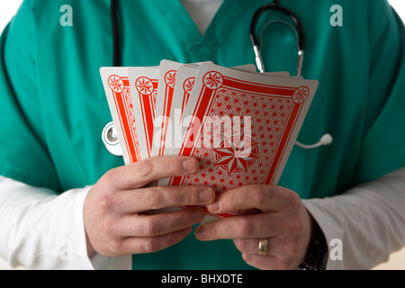 Uomo che indossa medical scrubs e uno stetoscopio in possesso di un set di carte da gioco Foto Stock