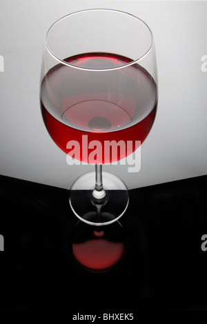 Vino rosso in un bicchiere sul grigio e sfondo nero con la riflessione Foto Stock