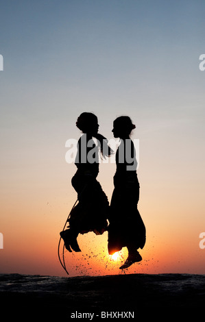 Silhouette di giovani ragazze indiano saltando in acqua al tramonto. India Foto Stock