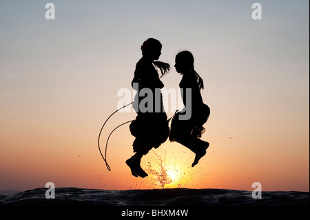 Silhouette di giovani ragazze indiano saltando in acqua al tramonto. India Foto Stock