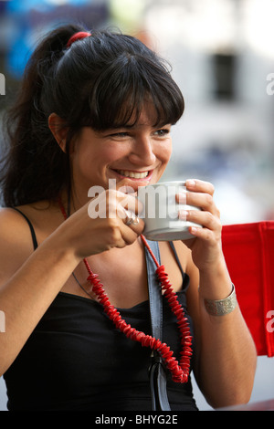 Metà anni venti ispanico donna sorridente su una tazza di caffè a un outdoor street cafe Foto Stock