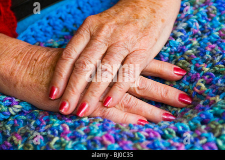 Invecchiamento Womans mani appoggiate sulla coperta di maglia. Foto Stock