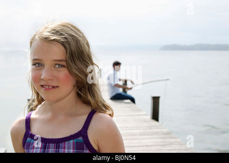 Ritratto di giovane ragazza sul molo con padre angling in background Foto Stock