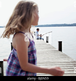 L'uomo angling sul molo con la giovane figlia in primo piano Foto Stock