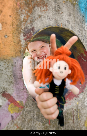 Ritratto di ragazza ridere guardando attraverso il foro nella parete sul parco giochi holding doll Foto Stock