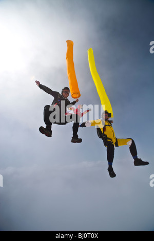 Skydivers con tubi colorati battenti intorno a ciascuna. Il Freeflyers si divertono nel cielo blu accanto a nuvole. Foto Stock