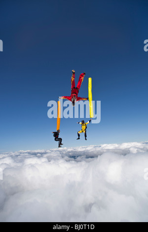 Skydivers con tubi colorati battenti intorno a ciascuna. Il Freeflyers si divertono nel cielo blu accanto a nuvole. Foto Stock