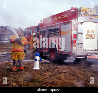 I vigili del fuoco e camion dei pompieri la spruzzatura di acqua su un incendio residenziali nel midwestern Stati Uniti d'America Foto Stock