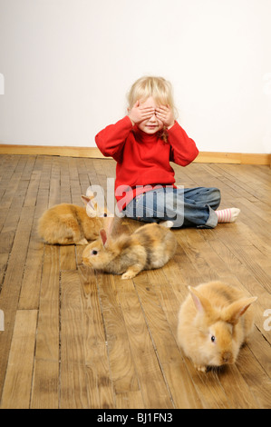 Foto di stock di un 4 anno vecchia ragazza giocando con il suo animale domestico dei conigli su un pavimento di legno. Foto Stock