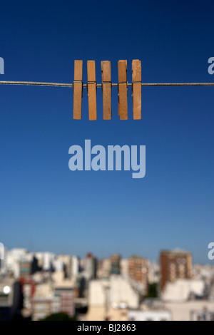 Cinque clothespegs close up appeso su una linea di lavaggio con il blu del cielo al di sopra dello skyline della città Foto Stock