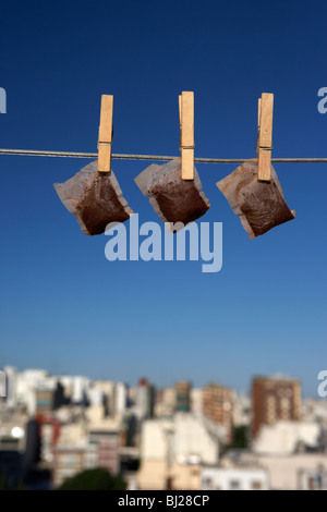 Tre teabags bagnato appeso su una linea di lavaggio con cielo blu su una skyline della città Foto Stock