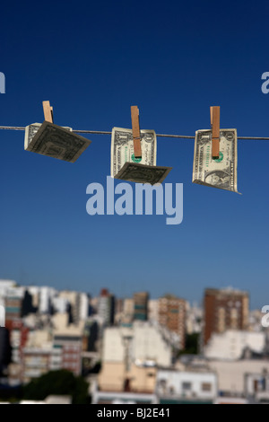 Tre le fatture del dollaro al vento appesi su una linea di lavaggio con cielo blu su una skyline della città Foto Stock