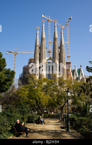 La gente seduta sulle panchine in un parco di fronte all'incompiuta Sagrada Familia a Barcellona in Spagna Foto Stock