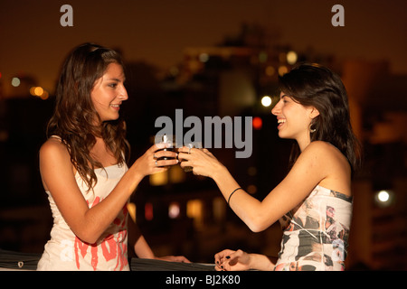 Due giovani ispanici donne latino bere birra e toccando i bicchieri insieme su un balcone party in buenos aires argentina Foto Stock