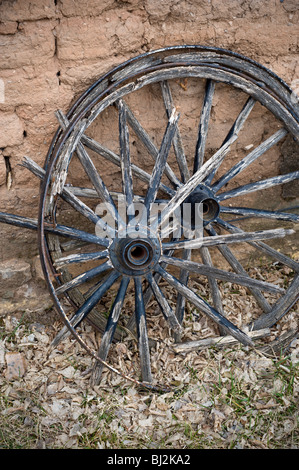 Il vecchio carro ruote in appoggio contro un mattone di adobe nel muro della storica città di Lincoln, Nuovo Messico. Foto Stock