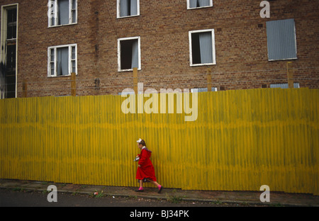 Una giovane ragazza cammina a metà strada lungo un tratto giallo brillante di lamiera corrugata in Toxteh, Liverpool 1991. Foto Stock