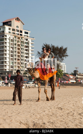 India Kerala, Calicut, Kozhikode beach, giovani turisti occidentali godendo di corsa in cammello sulla sabbia Foto Stock