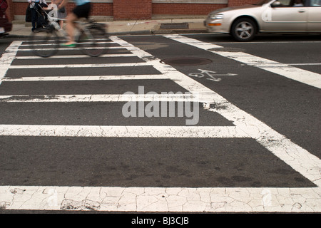 Una bicicletta whizzes attraverso le linee bianche indicano un percorso per i pedoni che attraversano la strada. Foto Stock