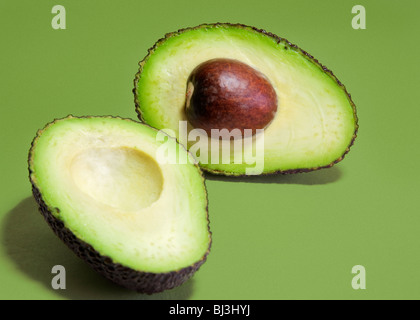 Varietà Hass avocado pera tagliata in due metà contro uno sfondo verde. Foto Stock