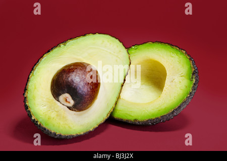 Varietà Hass avocado pera tagliata in due metà contro uno sfondo di colore rosso. Foto Stock