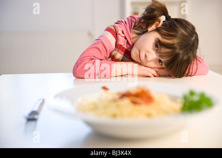 Bambina listlessly seduti davanti ad un piatto di spaghetti Foto Stock