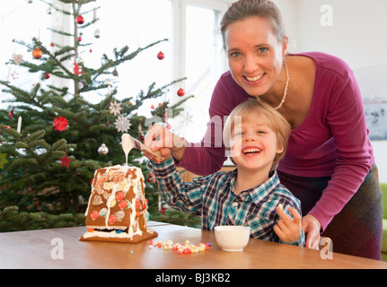 Madre, ragazzo decorare gingerbread house Foto Stock