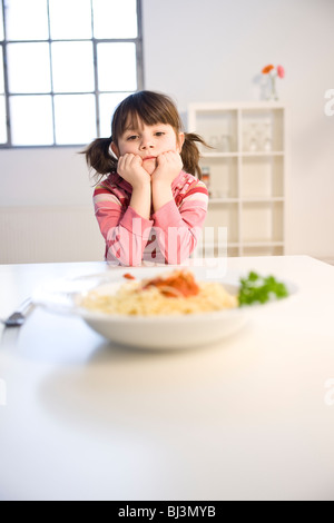 Bambina listlessly seduti davanti ad un piatto di spaghetti Foto Stock