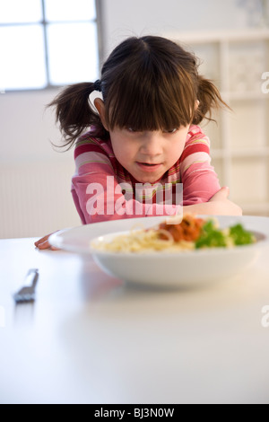 Bambina listlessly seduti davanti ad un piatto di spaghetti Foto Stock