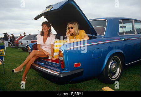 Due signore sedersi nel bagagliaio di azzurro splendente Rolls-Royce, chiacchierando e sorseggiando champagne da bicchieri di cristallo durante il Royal Ascot. Foto Stock