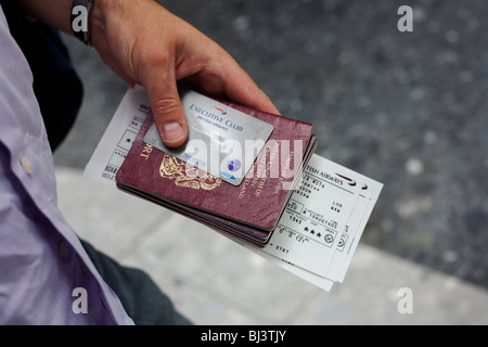 Close-up dettaglio di un maschio britannico del passeggero mano che tiene la sua famiglia viaggi di passaporti e documenti. Foto Stock