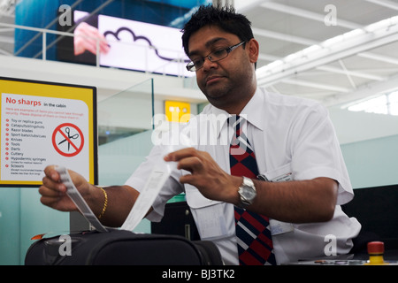 Un oggetti affilati avvertimento è di pianura a vedere come la British Airways check-in employee attribuisce una etichetta bagaglio a valigia del passeggero. Foto Stock