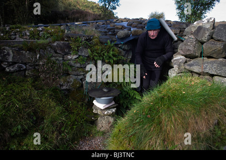 Tatuato eremita Tom Leppard emerge dall'ingresso del suo segreto rifugio improvvisato rifugio a Skye Foto Stock