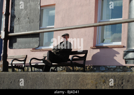 Il vecchio uomo su una panchina di fronte a casa rosa. Marine Parade, Lyme Regis, Dorset, Inghilterra Foto Stock