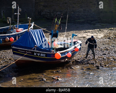 Un pescatore costiero controllando la sua barca su Roxby Beck Staithes North Yorkshire Foto Stock