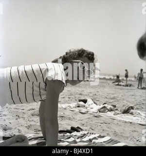 Moda donna in spiaggia durante gli anni cinquanta. sorridendo felice abito da sole Ombrelloni oceano atlantico bicchieri Foto Stock