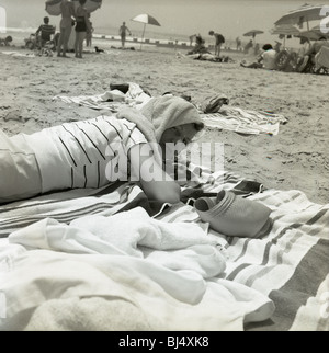 Moda donna in spiaggia durante gli anni cinquanta. sorridendo felice ombrelloni oceano atlantico testa di copertura della moda di asciugamani Foto Stock