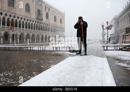 Un uomo si cancella la neve da passerelle in un invaso Piazza San Marco, Venezia, Italia Foto Stock