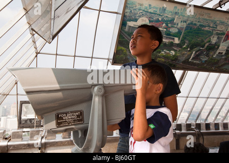 Indonesia, Java, Giacarta due bambini godendo di vista in elevazione dalla piattaforma di visualizzazione attraverso il binocolo Foto Stock