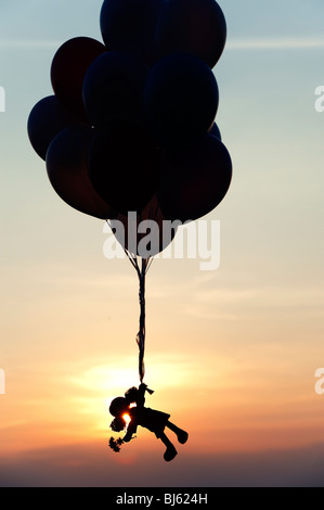 Rag Doll tenuta su palloni di elio che si allontanano al tramonto. Silhouette Foto Stock