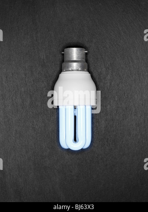 Cool blue energy saver lampadina luce su un grigio Sfondo ardesia Foto Stock