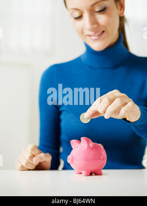Donna mettendo 1 euro in piccolo salvadanaio. Messa a fuoco selettiva, spazio di copia Foto Stock