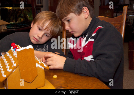 Età bambino 7 indossando REGNO UNITO Union Jack flag shirt e fratello età 10 decorazione di Natale casa di panpepato. St Paul Minnesota USA Foto Stock