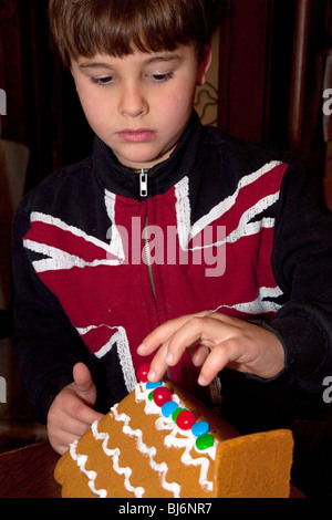 Ragazzo di 7 anni che indossa un REGNO UNITO Union Jack flag shirt decorare un Natale gingerbread house. St Paul Minnesota USA Foto Stock