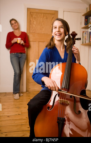 Ragazza pratica di suonare il violoncello a casa con la sua madre Foto Stock