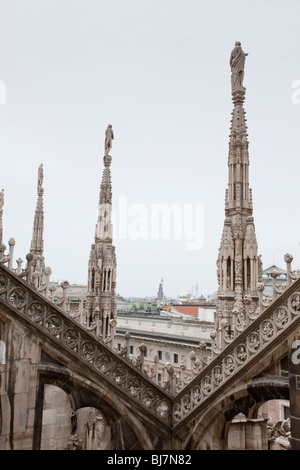 Le intricate guglie gotiche del Duomo di Milano si innalzano sopra la città, incorniciate da ornate pietre. Foto Stock
