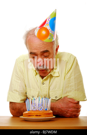 L'uomo soffiando fuori candele sessantacinquesimo compleanno Foto Stock