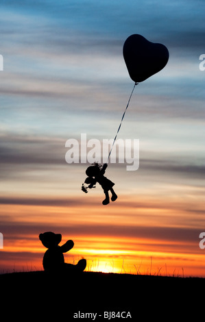 Rag Doll tenuta su di una forma di cuore palloncino elio che si allontanano da un orsacchiotto di sunrise. Regno Unito. Ancora vita silhouette Foto Stock