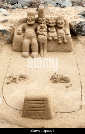 La scultura di sabbia di The Simpsons famiglia guardare la TV sul divano sulla spiaggia di Maspalomas gran canaria Foto Stock