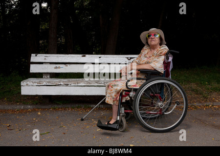 Donna anziana in carrozzina con funky occhiali da sole Foto Stock